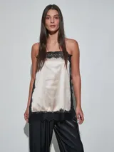 Musculosa de satén color beige claro, con detalles de encaje negro en el escote, los laterales y el ruedo, y tirantes finos.
