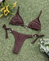 Conjunto de bikini color marrón chocolate, con corpiño triangular y bombacha colaless con tiras laterales para atar. Ambas piezas cuentan con argollas metálicas decorativas en el centro y los laterales.