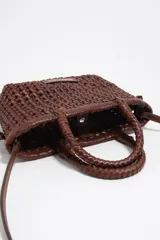Minibolso marrón de Bimba y Lola, confeccionado en piel vacuna con diseño trenzado y estructura rígida. Cuenta con asas de mano trenzadas, correa de hombro ajustable y etiqueta frontal con el logo de la marca.