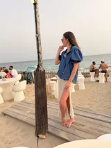 Camisa azul de denim liviano, de corte holgado y relajado, con mangas cortas abullonadas terminadas en volados y cierre frontal abotonado.