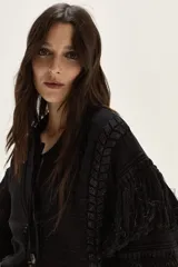 Cardigan de tejido de punto con detalles calados, trenzas y flecos en mangas y espalda. Presenta cierre frontal con botones, cuello redondo y mangas tres cuartos.