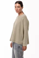 Remera de algodón color beige, con corte oversize, cuello redondo, mangas largas y detalle de puntilla en el ruedo.