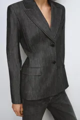 Blazer de mujer color gris oscuro, con efecto denim o tejido texturizado. Presenta cuello solapa de muescas, hombreras, bolsillos con solapa en el delantero y cierre frontal de dos botones oscuros.
