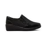 Zapato tipo slip-on de mujer en color negro, con diseño de textura combinada entre cuero mate y detalles en charol. Cuenta con un cierre lateral decorativo y funcional, y una suela de plataforma baja tipo cuña para mayor comodidad.