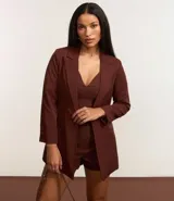 Blazer de sastrería color bordó, de corte oversized y largo, confeccionado en crepé. Presenta solapas clásicas, bolsillos frontales y detalle de pliegues en los puños.