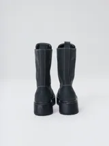 Botas de cuero color marrón de caña alta, con plataforma gruesa de goma y cierre metálico frontal con tirador. Presentan costuras a contratono y detalle de etiqueta de la marca en la lengüeta.