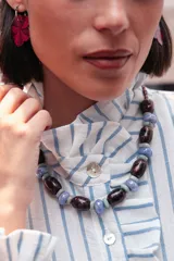 Collar corto compuesto por cuentas cilíndricas de color bordó con vetas oscuras, intercaladas con cuentas esféricas de cerámica en tonos celestes y grisáceos. Incluye cadena de ajuste metálica.
