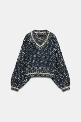 Jersey de punto con mezcla de hilos en tonos oscuros, blancos y azules, con escote en pico y manga larga. Presenta detalles de líneas en color crema en el cuello, puños y ruedo.
