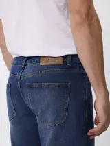 Jean de corte regular fit con tiro medio, confeccionado en denim de lavado oscuro con efecto localizado. Cuenta con diseño de cinco bolsillos, cierre frontal con cremallera y botón.