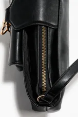 Cartera de hombro de diseño rectangular alargado, confeccionada en tejido revestido de color negro con herrajes metálicos dorados. Cuenta con un compartimento exterior con solapa y cierre de argolla metálica, cierre superior con cremallera y asa ajustable.
