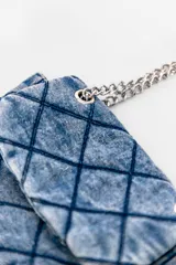 Cartera bandolera de jean negro con diseño acolchado en forma de rombos. Tiene correa de cadena plateada y manija de jean.