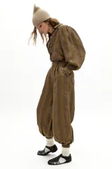 Pantalón de lino con diseño a rayas verticales en tonos tierra, de tiro medio y corte holgado. Presenta pretina con pasacintos, bolsillos laterales y traseros, y puños ajustados en los tobillos con botones de nácar.