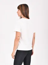 Remera lila de corte recto y mangas cortas, con estampado pequeño de un gato blanco con gorro rojo, gafas de sol y copa de vino, junto a la frase 'J'adore'.