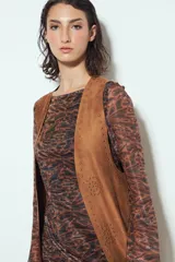 Chaleco largo de gamuza color marrón, con diseño abierto, flecos largos en el ruedo y apliques metálicos decorativos en el frente.