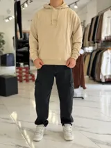 Canguro oversize beige con capucha y cordones ajustables, bolsillo tipo canguro y pequeño bordado en el pecho.