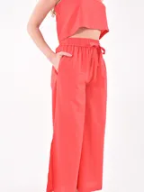 Pantalón de corte amplio y fluido, color rojo, con cintura elástica y cordón ajustable. Presenta aberturas laterales en el ruedo y bolsillos laterales.