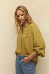 Camisa blanca de mangas abullonadas con sutiles plisados frontales, cuello clásico y corte relajado.