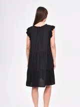 Vestido corto negro con estampado ikat en tonos marrones y beige. Presenta cuello en V con abertura y volados en las mangas cortas. Tiene un corte holgado con un volante en la parte inferior.