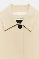 Chaqueta corta Zara ZW Collection de color beige, con cuello solapa, manga por debajo del codo, bolsillos laterales ocultos y cierre frontal con botones ocultos bajo solapa.