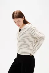 Sweater de punto a rayas horizontales color marrón y blanco, con cuello en V, capucha con cordones y cierre frontal parcial con botones. Presenta un diseño de manga larga con caída de hombros.