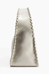 Cartera pequeña de color blanco hueso, con diseño rectangular y detalles entrelazados en los bordes y en el asa superior. Cuenta con cierre superior.