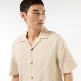 Camisa de manga corta color beige con cuello tipo campamento, cierre frontal de botones y diseño de textura en punto fantasía.