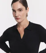 Blusa de punto ajustada color negro, con cuello polo y escote pronunciado en V. Presenta un tejido acanalado vertical en el torso y mangas largas.