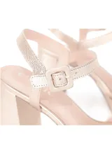 Sandalias de cuero color oro con taco de 10 cm y plataforma de 2 cm. Presentan tiras anchas cruzadas en la parte delantera y una tira fina con hebilla alrededor del tobillo.