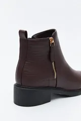 Bota corta de cuero sintético color negro, con taco bajo cuadrado y cierre lateral metálico. Presenta un detalle texturizado tipo reptil en la parte posterior del talón.