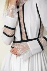 Vestido midi blanco con detalles de encaje y vivos negros. Tiene cuello mao, mangas largas con puños de encaje y falda amplia con tul de armar.