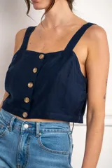 Top corto color rojo, con escote cuadrado y tirantes anchos. Presenta una hilera de botones marrones en el centro del frente.