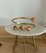 Conjunto de brazalete rígido y aros colgantes de bronce dorado, con incrustaciones de piedras irregulares en tonos ámbar con detalles de hoja de oro.