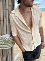 Camisa de manga corta confeccionada en tejido de punto con textura calada en patrón de espiga. Presenta cuello solapa, cierre frontal con botones y corte recto.