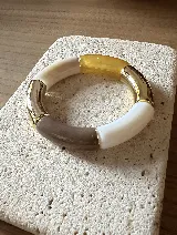 Pulsera elástica compuesta por piezas cilíndricas de acrílico en tonos beige, marrón, blanco y dorado.