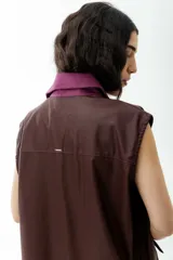 Chaleco marrón de cuerina con cuello de pana color lila, con bolsillos frontales y cierre con botones.