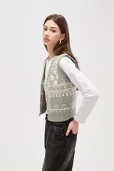 Chaleco tejido de punto con diseño jacquard de corazones y motivos geométricos en tonos verde y rosa. Presenta escote en V, cierre frontal con botones y terminaciones acanaladas en cuello, sisas y ruedo.