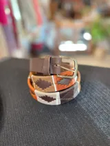 Cinturón de cuero en tono tostado con bordado a mano de hilos encerados en tonos marrones y beige con motivos geométricos, y hebilla metálica rectangular.