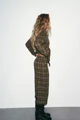 Pantalón bombacho de tiro medio con estampado a cuadros en tonos verde militar, negro y blanco. Presenta bolsillos laterales ocultos, cierre frontal con cremallera y botón, y bajo abullonado con puño y botón.