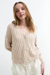 Cardigan beige de tejido calado con escote en V, manga larga y cierre frontal con tres botones.