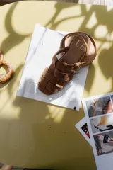 Sandalias de cuero marrón con diseño de tiras entretejidas y hebilla lateral.