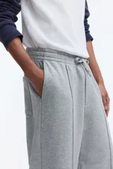 Pantalón jogger de punto de algodón gris melange, de corte relajado y perneras rectas con pliegue frontal cosido. Presenta cintura elástica con cordón ajustable, bolsillos laterales y falsas braguetas decorativas.