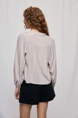 Blusa celeste de manga 3/4 con cuello mao, botonadura frontal y detalles calados en V con frunces. Presenta mangas con volumen y silueta fluida.