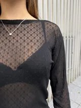 Polera de manga larga confeccionada en tela de encaje negro con textura geométrica. Presenta un diseño ajustado al cuerpo con cuello alto y acabado semitransparente.