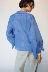 Camisa de cuello solapa y manga larga con detalle de lazos en los puños. Presenta un diseño de rayas verticales a tono y cierre frontal con botones ocultos.