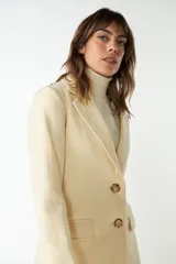 Blazer largo color crema con cuello solapa, bolsillos con solapa y forro interior combinado a tono. Confeccionado en lana fina sin teñir.