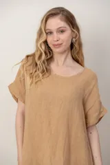 Vestido midi de lino color beige, de corte holgado y silueta acampanada. Cuenta con cuello redondo, mangas cortas amplias, bolsillos laterales y detalles de recortes horizontales en la falda con terminación asimétrica más larga en la parte trasera.