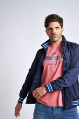 Campera liviana de nylon color gris oscuro, con cierre frontal completo, cuello subido y puños y cintura acanalados con rayas en rojo y blanco. Presenta logo bordado en el pecho y bolsillos laterales con cierre.