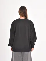 Buzo negro de corte holgado con cuello redondo y mangas largas con puños elásticos. Presenta un estampado frontal con la frase 'Shine Bright' en tipografía cursiva y texto complementario en blanco.