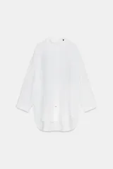 Camisa amplia de algodón con cuello redondo, manga por debajo del codo con puño y bajo asimétrico con aberturas laterales. Presenta cierre frontal con botones ocultos por solapa.