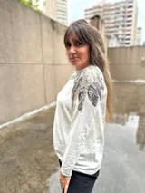 Buzo color crudo de mangas largas con apliques de lentejuelas plateadas y doradas en los hombros.